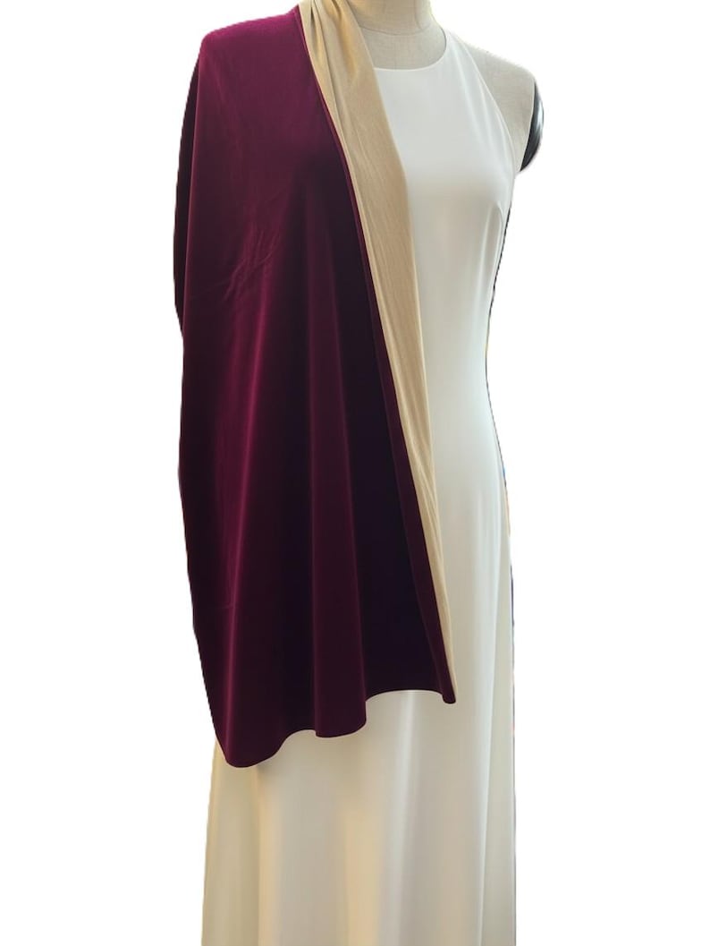 May include: A long, deep burgundy velvet shawl draped over a solid white sleeveless dress. The shawl features a smooth, rich texture and a contrasting beige lining visible along the folded edge, creating a layered look over the plain white gown.