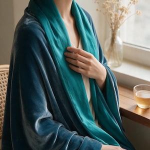 May include: A dual-toned wrap featuring a deep teal velvet exterior and a contrasting bright turquoise fabric interior. The garment drapes over the shoulders, showcasing a soft, reflective texture and a smooth, matte lining in a layered design.