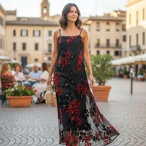 May include: A floor-length black slip dress featuring a sheer overlay with a vibrant red and black floral pattern, thin spaghetti straps, and a straight neckline. The dress has a relaxed, flowing silhouette that reaches down to the ankles.