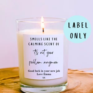 May include: A burning candle in a clear glass jar with a white label. The label says "Smells like the calming scent of it's not your problem anymore." The text "Good luck in your new job Love Emma XX" is also on the label. A light blue circle with the words "LABEL ONLY" is in the background.