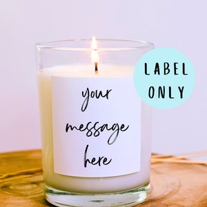 May include: A clear glass candle jar with a white label that says "your message here". The candle is lit and the flame is visible. The label is on a light blue background with the text "LABEL ONLY" in black.