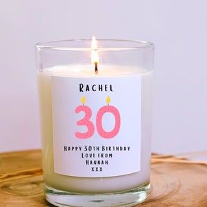 May include: A white candle in a clear glass jar with a pink and yellow birthday candle label that says "Rachel 30 Happy 30th Birthday Love from Hannah XXX"