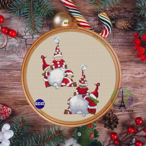 May include: Cross stitch pattern featuring three gnomes wearing red and white hats, holding a white snowball. The pattern is displayed in a wooden embroidery hoop.