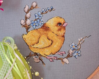 May include: A yellow chick embroidered on a blue fabric with white and blue flowers. The chick is sitting on a branch with pink feet.