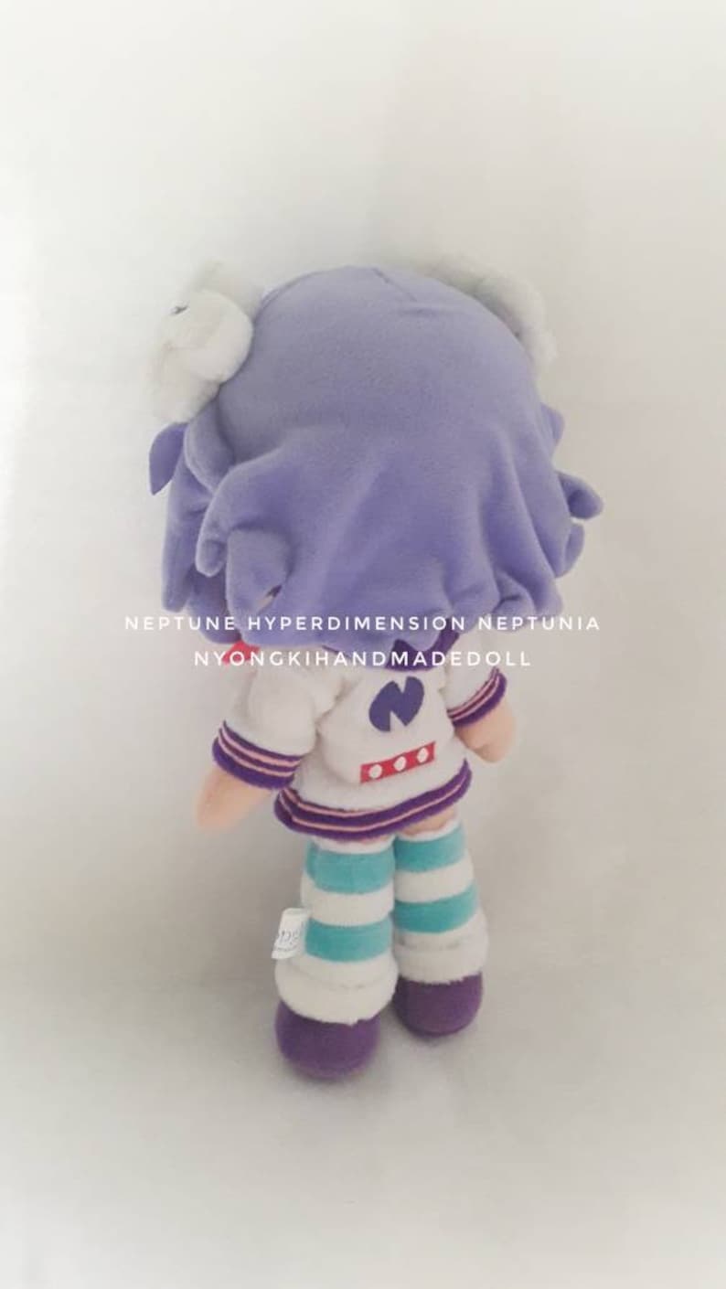 Puede incluir: Mu&ntilde;eca de peluche hecha a mano de un personaje de la serie Neptune Hyperdimension Neptunia. La mu&ntilde;eca tiene pelo morado, un atuendo blanco y azul y calcetines a rayas moradas y blancas. El texto "NYONGKIHANDMADEDOLL" es visible.