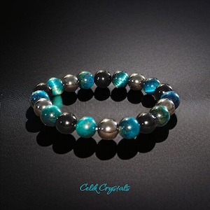 Op de afbeelding: Een armband gemaakt van blauwe tijgeroog, zwarte onyx en hematiet kralen. De armband ligt op een zwarte achtergrond.