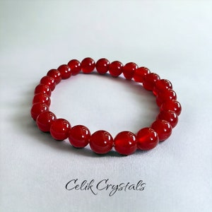 May include: A red carnelian gemstone bracelet with round beads. The bracelet is made of natural stones and is approximately 8 inches in length.