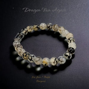 Puede incluir: Un brazalete de ágata de veta de dragón blanco y negro con cuentas redondas. El brazalete está hecho de piedra natural y tiene un patrón único.