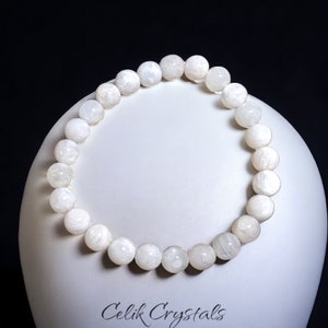 May include: White moonstone beaded bracelet. The bracelet is made of round, white beads with a smooth, polished finish. The beads are strung on a clear elastic cord.