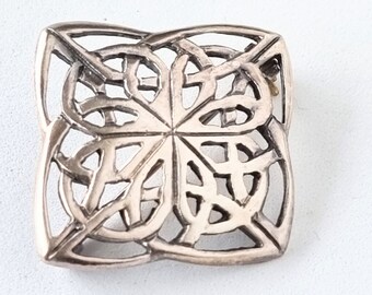 May include: A silver square-shaped brooch with a detailed Celtic knot design.