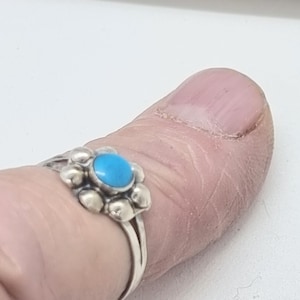 May include: A silver ring with a turquoise stone set in a flower design.