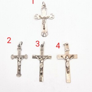 Puede incluir: Cuatro colgantes de crucifijo plateados, cada uno con una representación detallada de Jesucristo. Las cruces varían en diseño, con patrones intrincados y tamaños variables. Los colgantes se muestran sobre un fondo blanco liso.