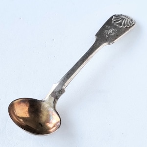 Pode incluir: Uma colher de sal de prata com uma tigela arredondada e um cabo decorativo. O cabo apresenta um design de concha e a inscrição "C.H.M."