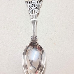 May include: A silver spoon with a floral design on the handle. The flowers are white with yellow centers and are arranged in a bouquet. The spoon is about 6 inches long.