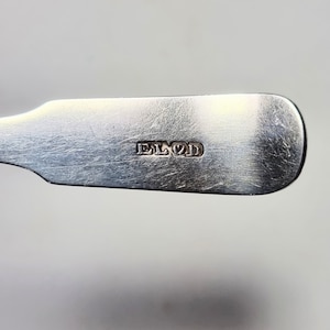 May include: Close-up of a silver spoon with the word "EL&D" engraved on the back.