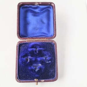 May include: An empty, vintage ring box with a brown leather exterior and a blue velvet interior. The box has four compartments for rings.