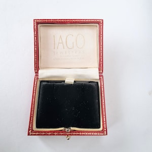May include: Red velvet jewelry box with gold trim and a black velvet interior. The box is open and the lid has the text "IAGO JEWELLERS 32 Falcon Street STRATFORD-ON-AVON" printed on it.