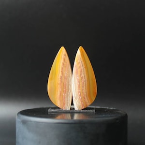 Pode incluir: Dois cabochões de ágata em forma de lágrima com um padrão em camadas de laranja, amarelo e branco.