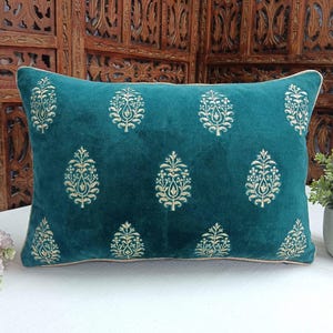 May include: Teal velvet pillow with gold embroidered floral pattern. The pillow has a white trim around the edges.