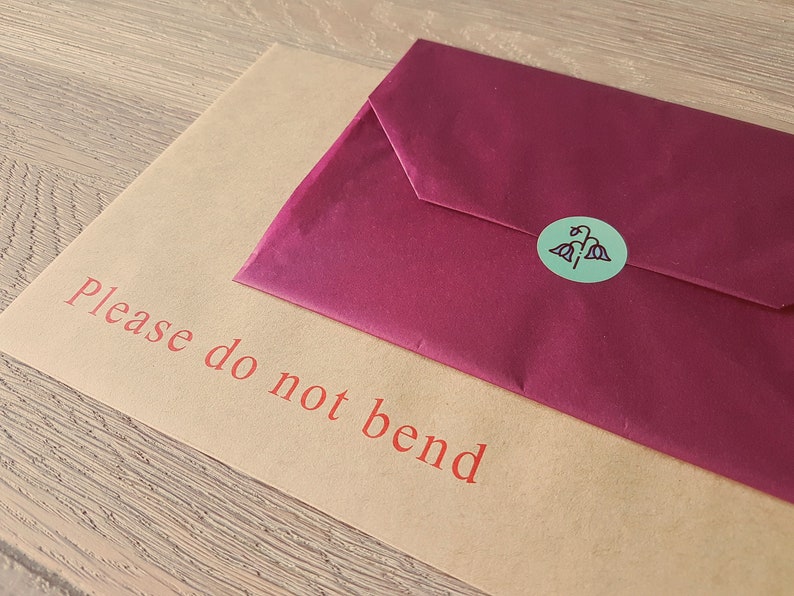 May include: A brown paper envelope with the text "Please do not bend" printed in red. A burgundy envelope is on top of the brown envelope with a green sticker with a floral design.