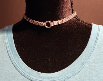 May include: A silver chain choker necklace with a round ring pendant. The necklace is on a black mannequin bust wearing a light blue t-shirt.