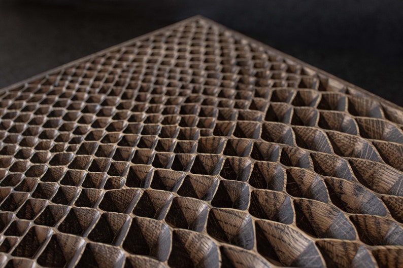 May include: Close-up of a wooden surface with a repeating geometric pattern. The pattern consists of small, raised, pyramid-shaped blocks arranged in a grid. The wood has a dark brown color with visible grain.