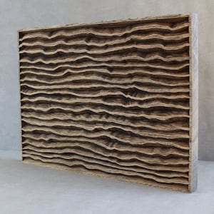 Op de afbeelding: Een rechthoekig houten wandkunstwerk met een getextureerd, gelaagd ontwerp. Het kunstwerk heeft horizontale, golfachtige patronen die in het hout zijn gesneden, waardoor een driedimensionaal effect ontstaat. Het hout heeft een natuurlijke, lichtbruine kleur.
