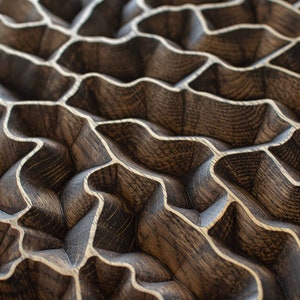 May include: Close-up of a wooden surface with a repeating, wave-like pattern. The wood has a dark brown stain with lighter, natural wood grain accents. The design creates a textured, three-dimensional effect.