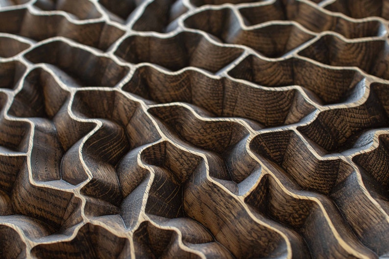 May include: Close-up of a wooden surface with a repeating, wave-like pattern. The wood has a dark brown stain with lighter, natural wood grain accents. The design creates a textured, three-dimensional effect.