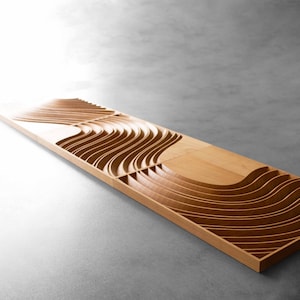 May include: A wooden wall panel with a carved design of overlapping waves. The panel is made of light brown wood and has a natural finish.