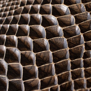 May include: Close-up of a textured, dark brown wooden surface with a repeating geometric pattern. The pattern consists of square-shaped blocks with beveled edges, creating a three-dimensional effect. The wood grain is visible.