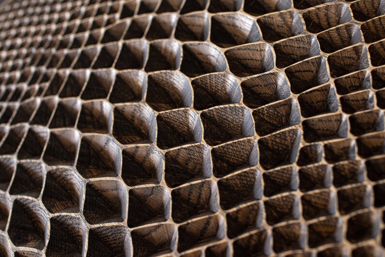 May include: Close-up of a textured, dark brown wooden surface with a repeating geometric pattern. The pattern consists of square-shaped blocks with beveled edges, creating a three-dimensional effect. The wood grain is visible.
