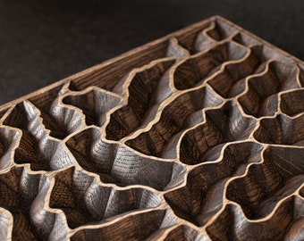 May include: Close-up of a handcrafted wooden tray with a unique, carved topographic design. The tray features a dark brown finish with lighter wood accents, creating a textured, three-dimensional effect. The design resembles a stylized landscape.