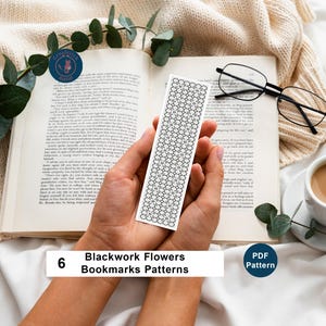 May include: A white bookmark with a black floral pattern is held over an open book. The bookmark features a repeating design of black flowers. The text "6 Blackwork Flowers Bookmarks Patterns" is visible. A cup of coffee and glasses are also in the image.