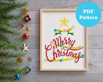 May include: A cross-stitch pattern featuring a Christmas tree with the words "Merry Christmas" in red lettering. The tree is decorated with yellow, pink, and blue ornaments. The pattern is in a wooden frame.