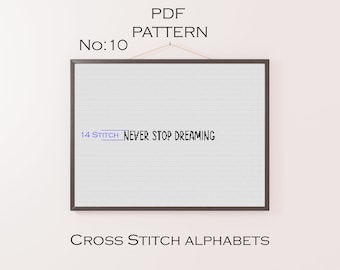 Może przedstawiać: Wzorzec haftu krzyżykowego w ramie z tekstem "NEVER STOP DREAMING" i "14 STITCH" w niebieskim polu. Wzór jest w czarnej ramie i wisi na białej ścianie. Tekst "PDF PATTERN No: 10" znajduje się nad ramą, a tekst "CROSS STITCH ALPHABETS" pod ramą.