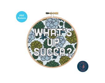 Może przedstawiać: Wzór do haftu krzyżykowego z motywem kwiatowym i tekstem "What's Up Succa?" w białych literach. Wzór jest w okrągłym obręczy.