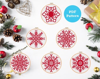 Puede incluir: Seis patrones de punto de cruz de copo de nieve rojo en aros de bordado sobre un fondo blanco. El texto "PDF Pattern" está en un círculo azul.