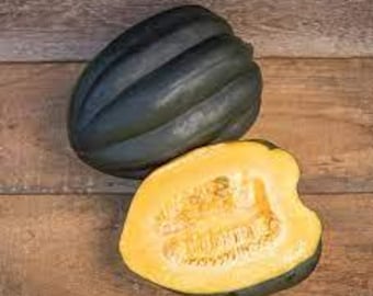 May include: Two acorn squashes on a wooden surface. One is whole, dark green, and ridged. The other is cut in half, revealing bright yellow flesh and seeds.