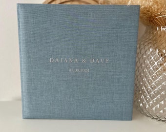 Op de afbeelding: Een lichtblauw fotoalbum met een linnenstructuur en de tekst "DAJANA & DAVE 07.09.2024" in wit gedrukt.