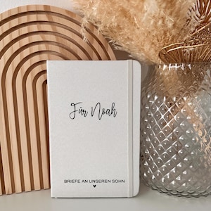 Könnte beinhalten: Ein weißes Notizbuch mit dem Text "Für Noah" und "Briefe an unseren Sohn" mit einem kleinen Herzsymbol.