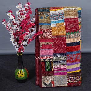 Könnte beinhalten: Ein Patchwork-Quilt mit einer Vielzahl von bunten Stoffquadraten. Der Quilt weist eine Mischung aus Mustern und Texturen auf, darunter Blumendrucke und unifarbene Farben. Der Text "Countdown Mart" ist auf dem Quilt zu sehen. Eine Vase mit Blumen befindet sich links.