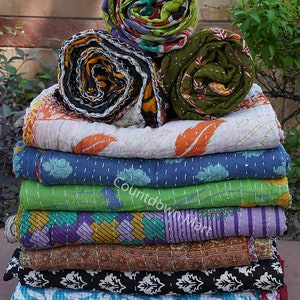 May include: A stack of 11 kantha quilts in various colors and patterns, including floral, geometric, and paisley designs. The quilts are folded and stacked on top of each other, with the top three quilts rolled up.