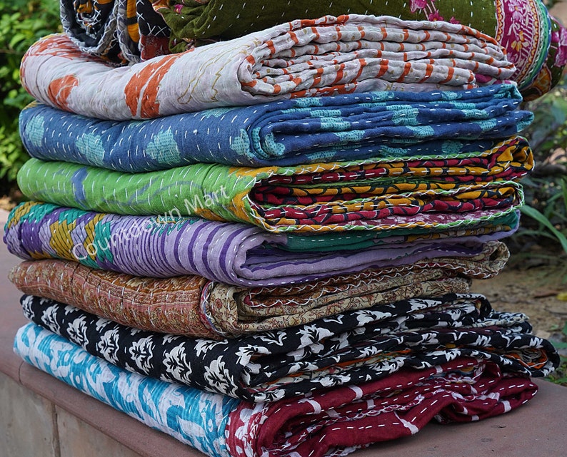 May include: A stack of colorful kantha quilts, a traditional Indian textile, with various patterns and stitching. The quilts are folded and stacked on top of each other, creating a visually appealing display.