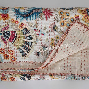 Może przedstawiać: Biała bawełniana kołdra kantha z kwiatowym i paisleyowym wzorem w odcieniach czerwieni, żółci, błękitu i zieleni. Kołdra jest złożona na pół i ma czerwony ścieg wokół krawędzi.