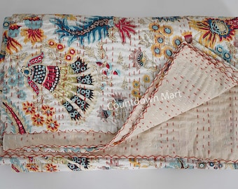 May include: A white cotton kantha quilt with a floral and paisley pattern in shades of red, yellow, blue, and green. The quilt is folded in half and has a red stitching detail around the edges.