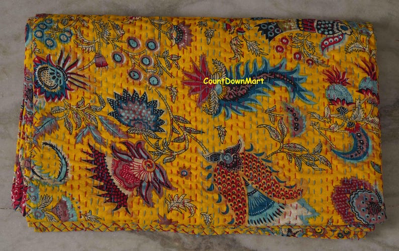Peut inclure: Textile jaune pli&eacute; avec un motif floral dans les tons de bleu, rouge et blanc. Le textile a un aspect matelass&eacute; avec des coutures visibles. Le texte "CountDownMart" est visible sur le textile.