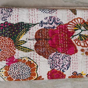 May include: A folded white quilt with a colorful floral pattern. The design includes large flowers in shades of pink, orange, and brown, with green and yellow leaves. The quilt is stitched with red thread.