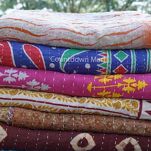 May include: A stack of six colorful kantha quilts with various patterns, including floral, geometric, and paisley designs. The quilts are made of cotton and are hand-stitched. The quilts are folded and stacked on top of each other. The text "Countdown Market" is visible on the second quilt from the top.