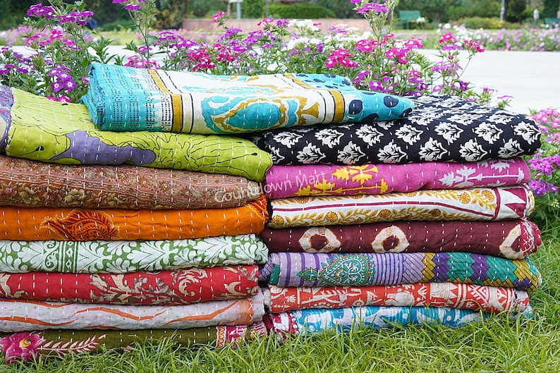 May include: A stack of colorful kantha quilts with various patterns and designs. The quilts are made of cotton and are hand-stitched. They are perfect for adding a touch of bohemian style to any room.